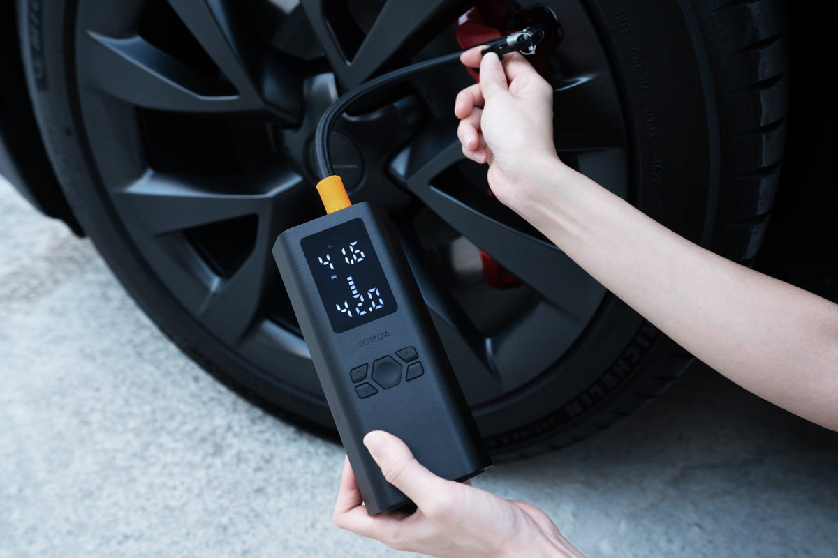Kéz tartja a légkompresszort, miközben a Tesla kerekénél pumpál, a kijelzőn a kívánt és a tényleges nyomás látható
