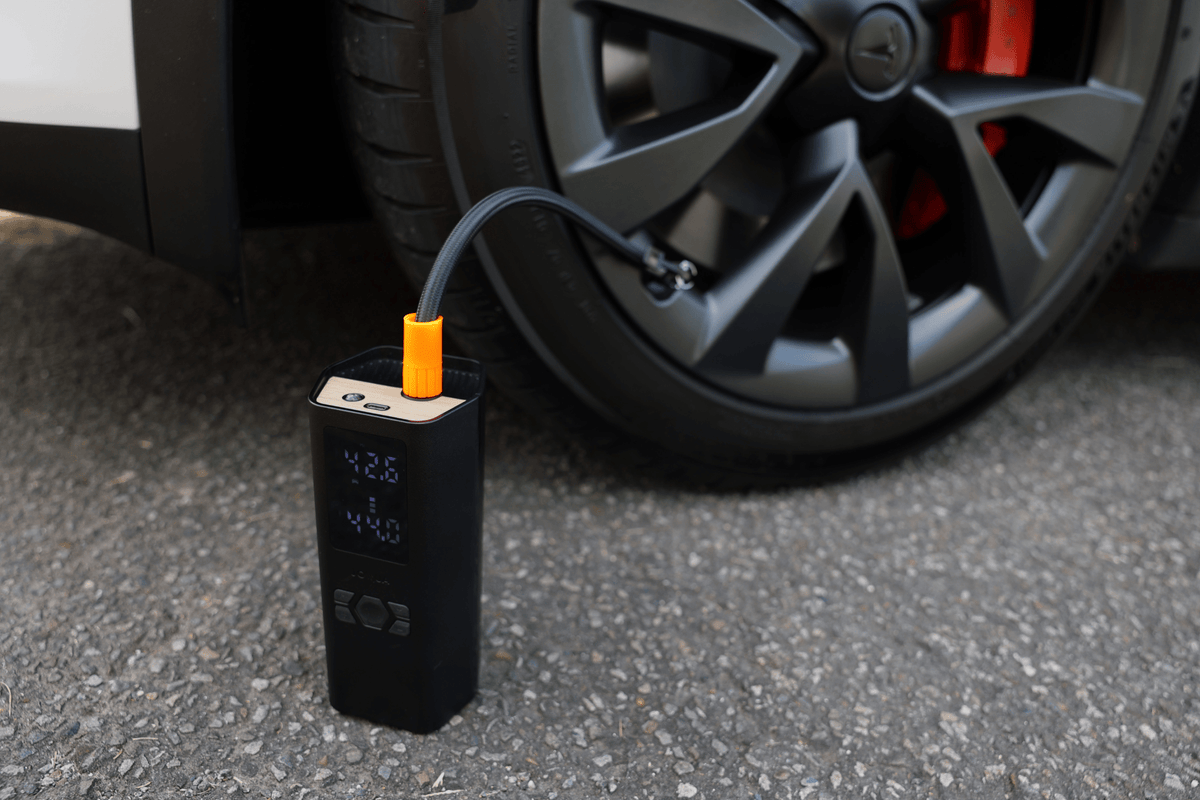 A légkompresszor a Tesla kerekénél áll, és a csatlakoztatott csövön keresztül pumpálja a gumit
