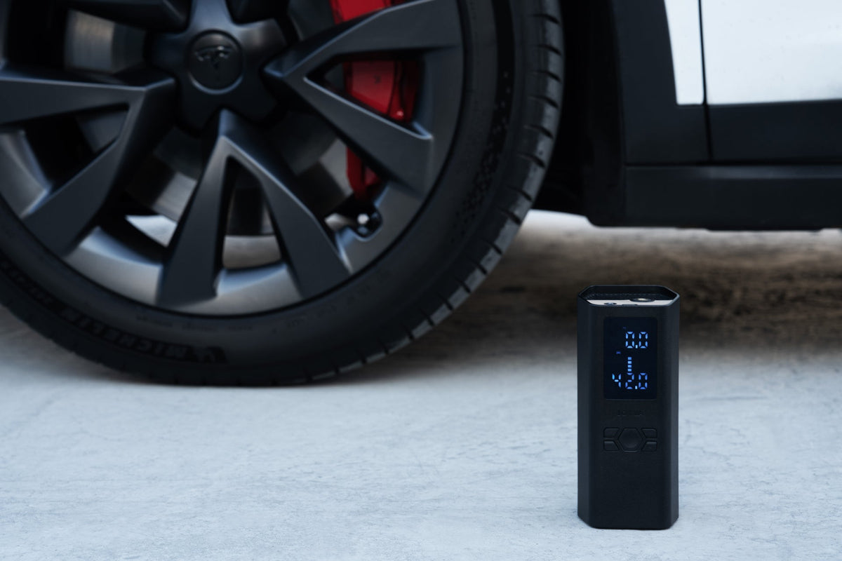 A hordozható légkompresszor a Tesla kerekénél áll az aszfalton